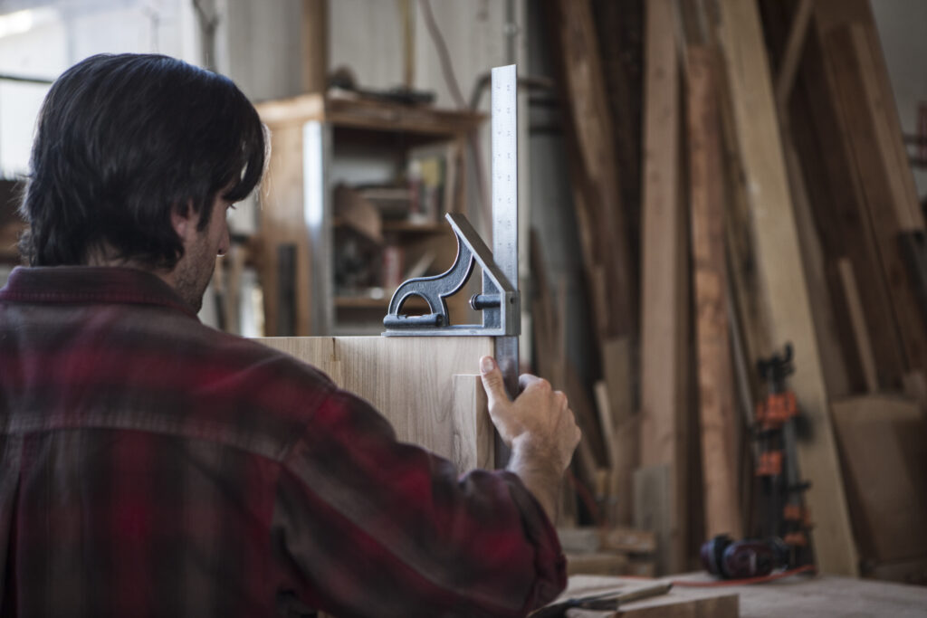 Artigiano al lavoro in falegnameria mentre misura un pannello in legno, simbolo della professionalità di un mobiliere moderno a Napoli.