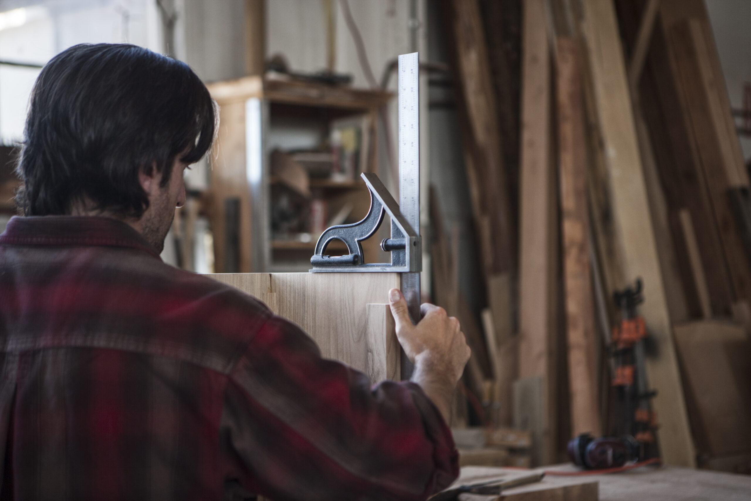 Artigiano al lavoro in falegnameria mentre misura un pannello in legno, simbolo della professionalità di un mobiliere moderno a Napoli.